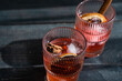 © RooM The Agency - Close-up of two cherry cocktails with cinnamon sticks and dried orange slices on a wooden table in the sunlight