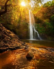 Canvas Print - Golden hour at a breathtaking waterfall. Sunlight illuminates the cascading water and lush greenery.