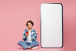 © ViDi Studio - Full body young woman she wear blue shirt white t-shirt casual clothes sit point on big huge blank screen mobile cell phone with area using smartphone isolated on plain pastel light pink background.