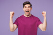 © ViDi Studio - Young Caucasian man he wears violet t-shirt casual clothes doing winner gesture celebrate clenching fists say yes isolated on plain pastel light purple background studio portrait. Lifestyle concept.