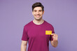 © ViDi Studio - Young smiling happy Caucasian man he wears violet t-shirt casual clothes hold in hand mock up of credit bank card isolated on plain pastel light purple background studio portrait. Lifestyle concept.