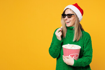 Wall Mural - Young merry woman wear green casual sweater 3d glasses watch movie film hold bucket of popcorn in cinema look aside area isolated on plain yellow background. Happy New Year, Christmas holiday concept.