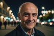 © ThomasLENNE - Close portrait of a smiling senior Albanian man looking at the camera, Albanian city outdoors at night blurred background