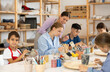 © JackF - Teenagers and children at a ceramics workshop in an art studio. Woman teacher shows how to paint clay dishes with a brush