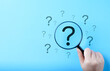 © Supatman - Question Mark and Root Cause Analysis Concept. A hand holding a magnifying glass over a large question mark surrounded by smaller ones on a blue background, symbolizing analysis and problem-solving.