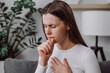 © Yura Yarema - Ill upset young caucasian woman sitting on couch freezing blowing running nose got fever cough cold sneezing, sick female having influenza symptoms coughing at home, flu concept
