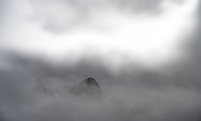 A rocky mountain peak jutting out of the mist and clouds with transparent areas
