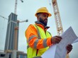 © useful pictures - A construction worker examines blueprints on a city site during cloudy weather while tall cranes work in the background