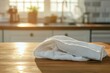 © raja - A white kitchen towel folded on a wooden table with a blurred kitchen background.