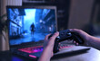 © Stanisic Vladimir - Player holding a gamepad in front of a gaming laptop displaying an action game, highlighting portable gaming setups and dynamic entertainment experiences