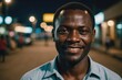 © ThomasLENNE - Close portrait of a smiling 40s Beninese man looking at the camera, Beninese city outdoors at night blurred background