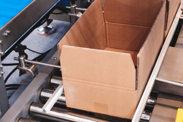 Poster - A brown cardboard box is sitting on a conveyor belt in a factory. The box is positioned in the middle of the conveyor belt, and it is in the process of being loaded or unloaded