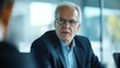 © Lion - elderly businessman in a suit speaking in a meeting, serious expression, well-lit modern office