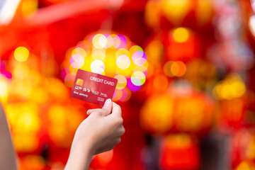 Wall Mural - Business financial and cashless payment concept. Woman hand holding credit card shopping at Chinatown street market in the city. Happy Asian people enjoy celebration Chinese lunar new year festival.