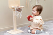 © Irina Mikhailichenko - Little baby toddler girl in beige bodysuit sitting with soft ball on a floor near wooden basket and playing basketball in children room. High quality photo