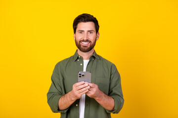 Wall Mural - Portrait of nice young man hold phone wear khaki shirt isolated on yellow color background