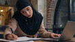 © Yuliia - Muslim woman in hijab female office manager businesswoman consult client talk mobile phone at business company Arabian islamic girl freelancer student working with laptop computer write notes at cafe
