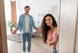 © Prostock-studio - Portrait of cheerful couple inviting guests to enter home, happy people standing in doorway of modern flat, looking out waiting for visitor to come in, receiving friend, lady peeking out of front door