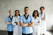 © Prostock-studio - International team of doctors posing together while having morning breefing, male and female medical workers standing against wall, holding arms crossed on chests, cheerfully smiling at camera
