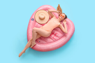 Wall Mural - Beautiful young happy woman in swimsuit lying on inflatable mattress against blue background