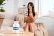 © Pixel-Shot - Young woman taking pills at home, focus on bottle with vitamin B