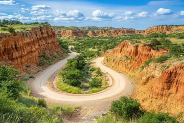 A winding dirt road through rugged, colorful canyon landscapes under a bright blue sky.