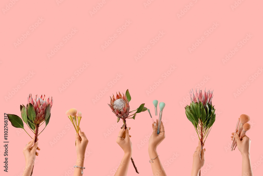 Hands with makeup brushes and protea flowers on pink background