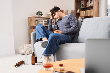 Wall Mural - Drunk young man with whiskey sitting on sofa at home. Alcoholism concept