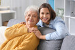 © Pixel-Shot - Young nurse hugging senior woman on sofa at home