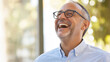© fangphotolia - Joyful Mature Man: Portrait of a happy middle-aged man with glasses laughing heartily, radiating positive energy and good vibes.