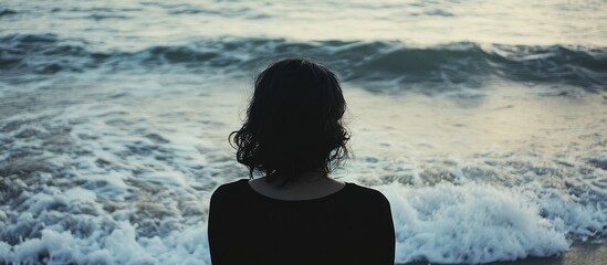 Poster - Reflective silhouette of a woman by the sea at sunset with gentle waves creating a tranquil and serene atmosphere