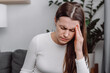 © Yura Yarema - Tired unhealthy young woman sitting alone on couch in living room at home with closed eyes, holding head with hand, suffering from strong sudden headache or migraine, throbbing pain concept