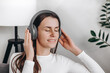 © Yura Yarema - Positive relaxed young female wearing wireless headphones sitting on couch, listening to songs from online playlist, musical Internet service, media application, relaxing at home