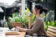 © bongkarn - A beautiful, calm Asian woman enjoys a hot drink while working remotely from a coffee shop.