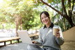 © bongkarn - A woman enjoys a hot drink while working remotely outdoors, sits on a park bench with her laptop.