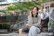 © bongkarn - A cheerful Asian woman sits outdoors, laughing and enjoying a fun conversation on the phone.
