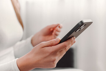 Close up of female hands holding credit card and smartphone sitting on sofa, paying online, using banking service, entering information, shopping, ordering in internet store, doing secure payment