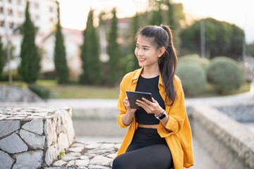 Wall Mural - Smiling young Asian woman using digital tablet in urban city