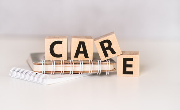 Text Care on wooden block with notebook on gray background.
