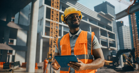 Portrait of a Handsome Black Civil Engineer Working on a Tablet at a Construction Site. Young African Man Standing Outdoors, Using Computer Device for Planning and Developing a Real Estate Project