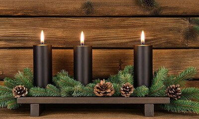 Wall Mural - Three tall black candles placed on a rustic wooden display surrounded by greenery and pinecones create a warm and inviting atmosphere