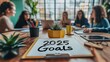 © Lamina - Close-up of a '2025 Goals' signboard on a vibrant desk with plants, notebooks, and team members collaborating in the background.