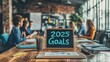 © Lamina - Workspace with a '2025 Goals' signboard on a wooden table, surrounded by focused team members in a creative and collaborative environment.