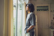 © JR-50 - Thoughtful Asian Man Gazing Out Window in Cozy, Sunlit Home Interio