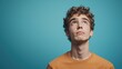 © Thuntaree - Pensive Young Man with Curly Hair Against a Blue Background
