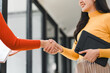 © kenchiro168 - woman in yellow sweater shakes hands with another person, holding tablet. scene reflects professional interaction, showcasing collaboration and engagement