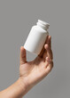 © katrinshine - Female hand holding a white plastic pill bottle closeup against grey, Healthcare concept