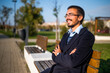 © inesbazdar - Portrait of content young businessman with arms crossed looking away while sitting on the bench in the park on a sunny autumn day. He is resting and thinking about something.