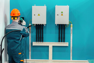 Poster - electrician installs power panels on wall. electrical engineer stands to camera. electrical panels w