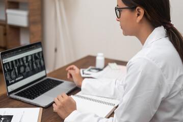 Aufkleber - Radiology Review: A young doctor in glasses examines X-ray images displayed on a laptop screen with a focused gaze.